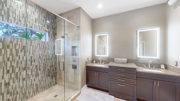 Modern bathroom with a tiled shower, two sinks with backlit mirrors, and dark brown cabinets.