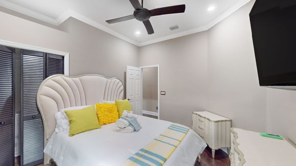 Bedroom with a large ornate headboard, yellow pillows, and a decorative blanket. A ceiling fan and a dresser are also visible.