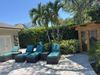 Lounge chairs on a patio near a small wooden structure, under palm trees and a clear sky.