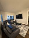A modern living room with a grey sectional sofa, a mounted TV, and a round coffee table on a fluffy grey rug.