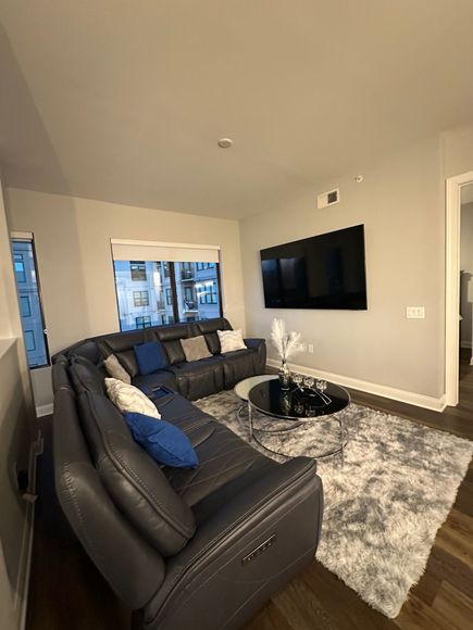 A modern living room featuring a sectional sofa, a mounted TV, and a round coffee table on a fluffy gray rug.