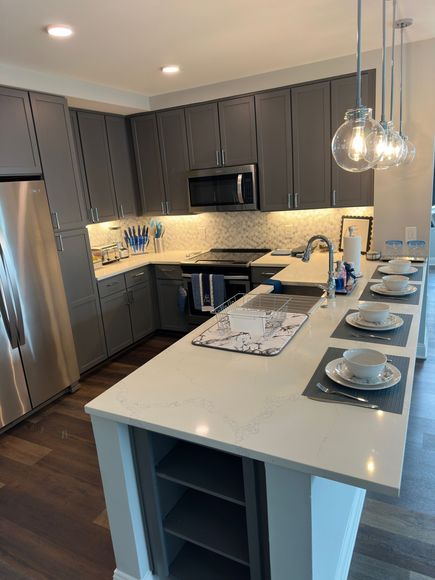 Modern kitchen with gray cabinets, stainless steel appliances, a white countertop island, and pendant lights.