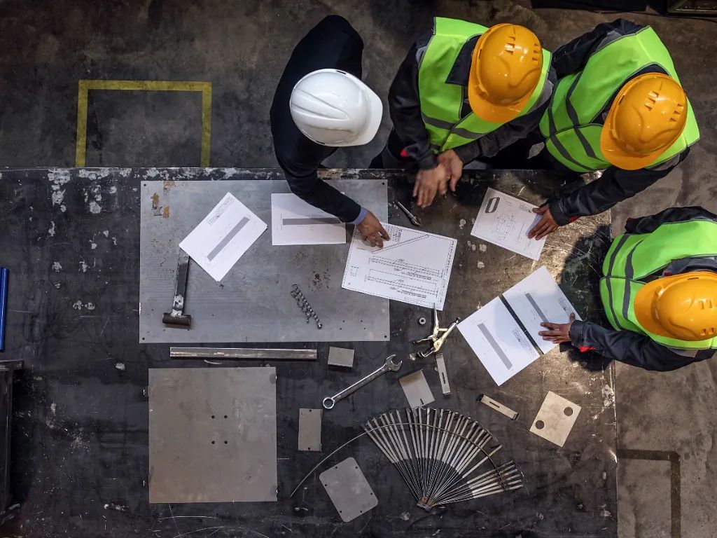 Un grupo de trabajadores de la construcción están sentados alrededor de una mesa mirando papeles.