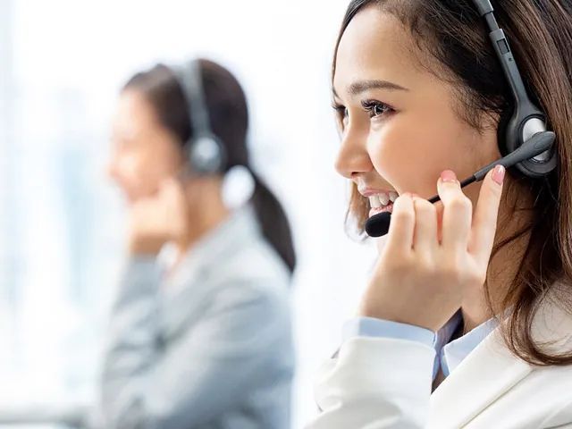 Una mujer que usa unos auriculares está hablando por teléfono en un centro de llamadas.