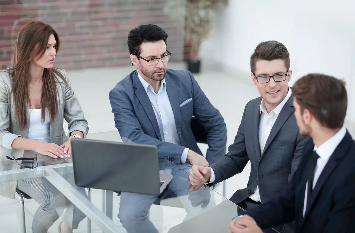 Un grupo de hombres de negocios están sentados alrededor de una mesa dándose la mano.