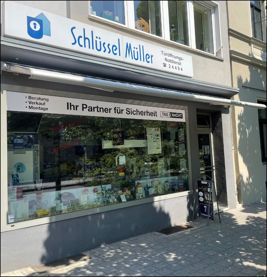 Schaufensterfront des Schlüsseldienstes „Schlüssel Müller“ mit weißer Markise und Schaufensterauslagen an einer sonnigen Straße