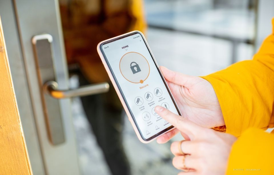 Eine Person benutzt eine Smartphone-App, um eine Tür mit einem intelligenten Schloss zu entriegeln.