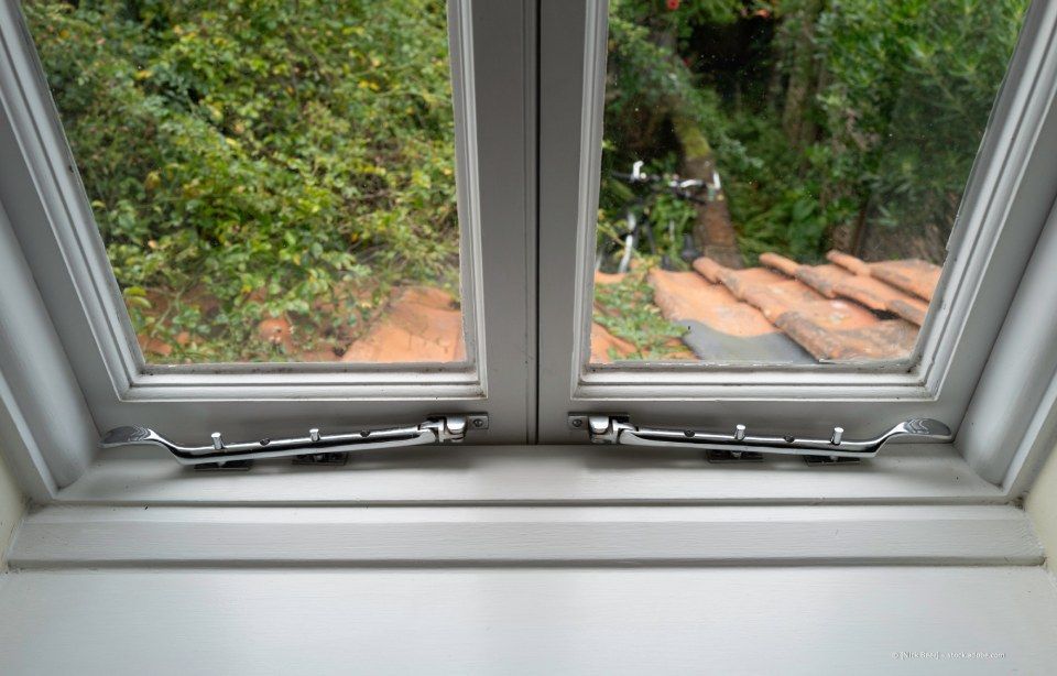Offenes Fenster mit Blick auf einen üppigen Garten mit Terrakottafliesen und viel Grün draußen