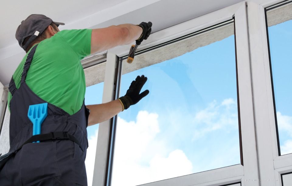 Arbeiter putzt an einem hellen Tag ein Fenster mit einem Abzieher.