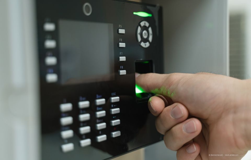 Eine Hand drückt einen leuchtenden Fingerabdruckscanner auf ein schwarzes Zutrittskontrollpanel.