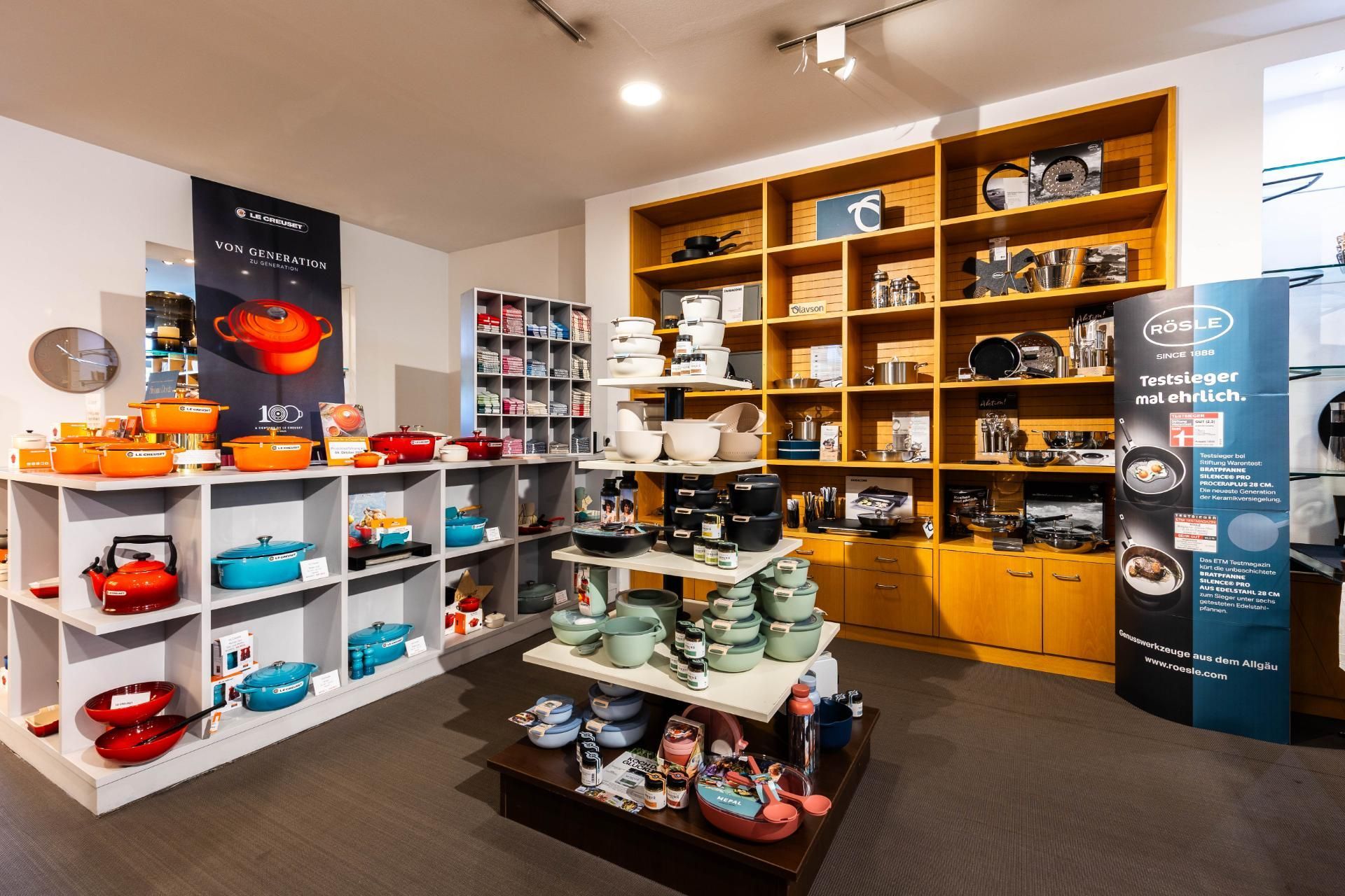 Innenansicht eines Kochgeschirrgeschäfts mit Regalen voller bunter Töpfe, Kessel und anderer Küchenartikel.