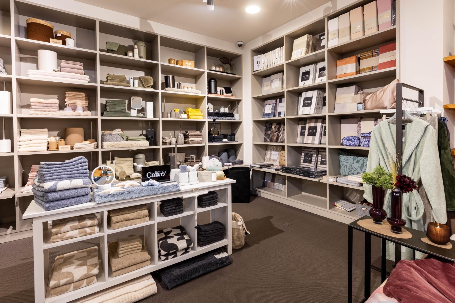 Innenansicht eines Einzelhandelsgeschäfts mit Regalen voller Textilien und Haushaltswaren und einem Tisch mit Auslage.