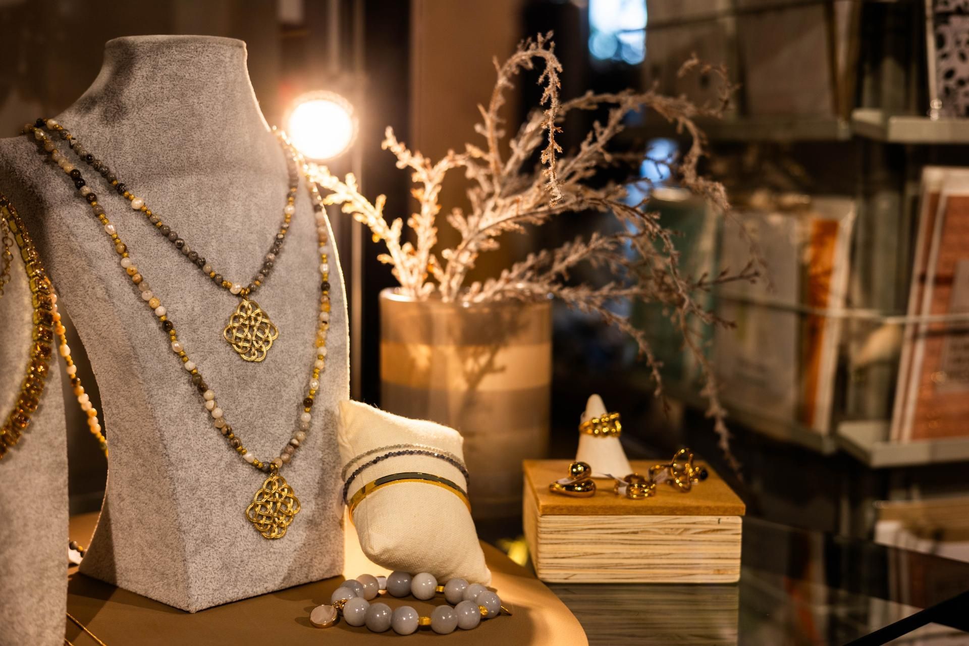 Schmuckdisplay mit Halsketten, Armbändern und Ringen auf Schaufensterpuppen und einer Holzkiste. Sanfte Beleuchtung.