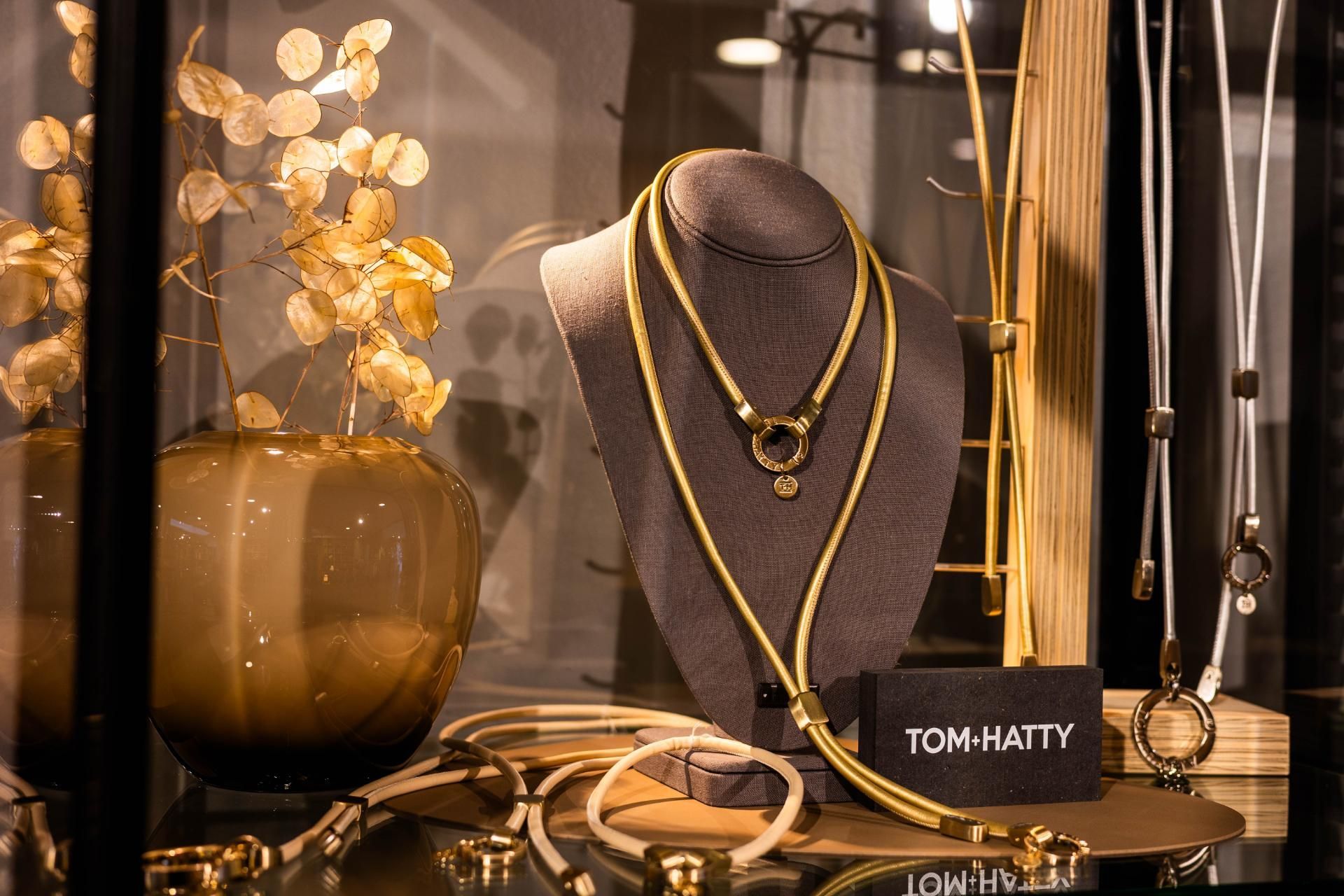 Schmuckvitrine mit goldenen Halsketten und einer Vase mit goldenen Blättern.