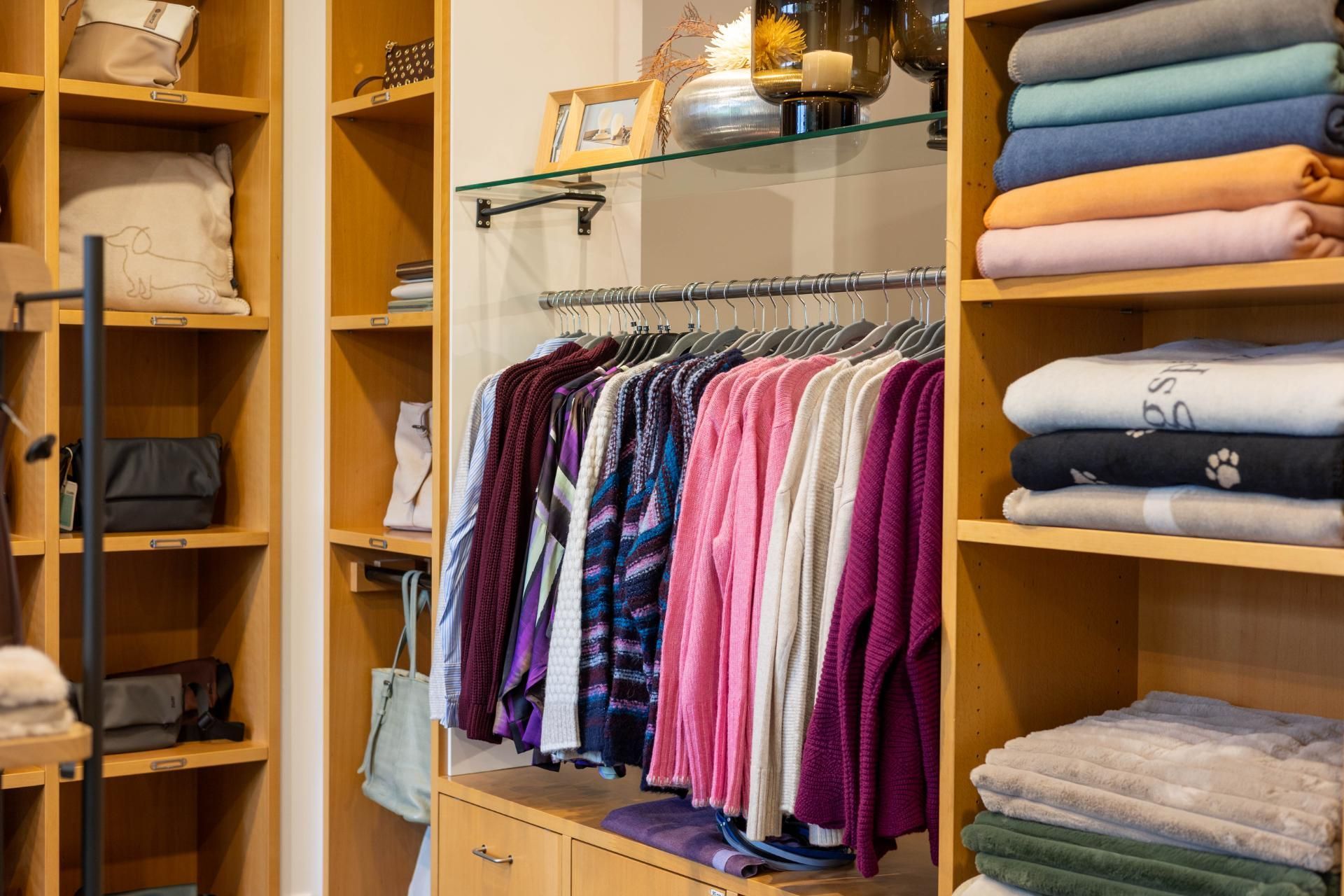 Innenansicht eines Bekleidungsgeschäfts mit Regalen voller gefalteter Pullover, hängenden Hemden und Warenauslagen.