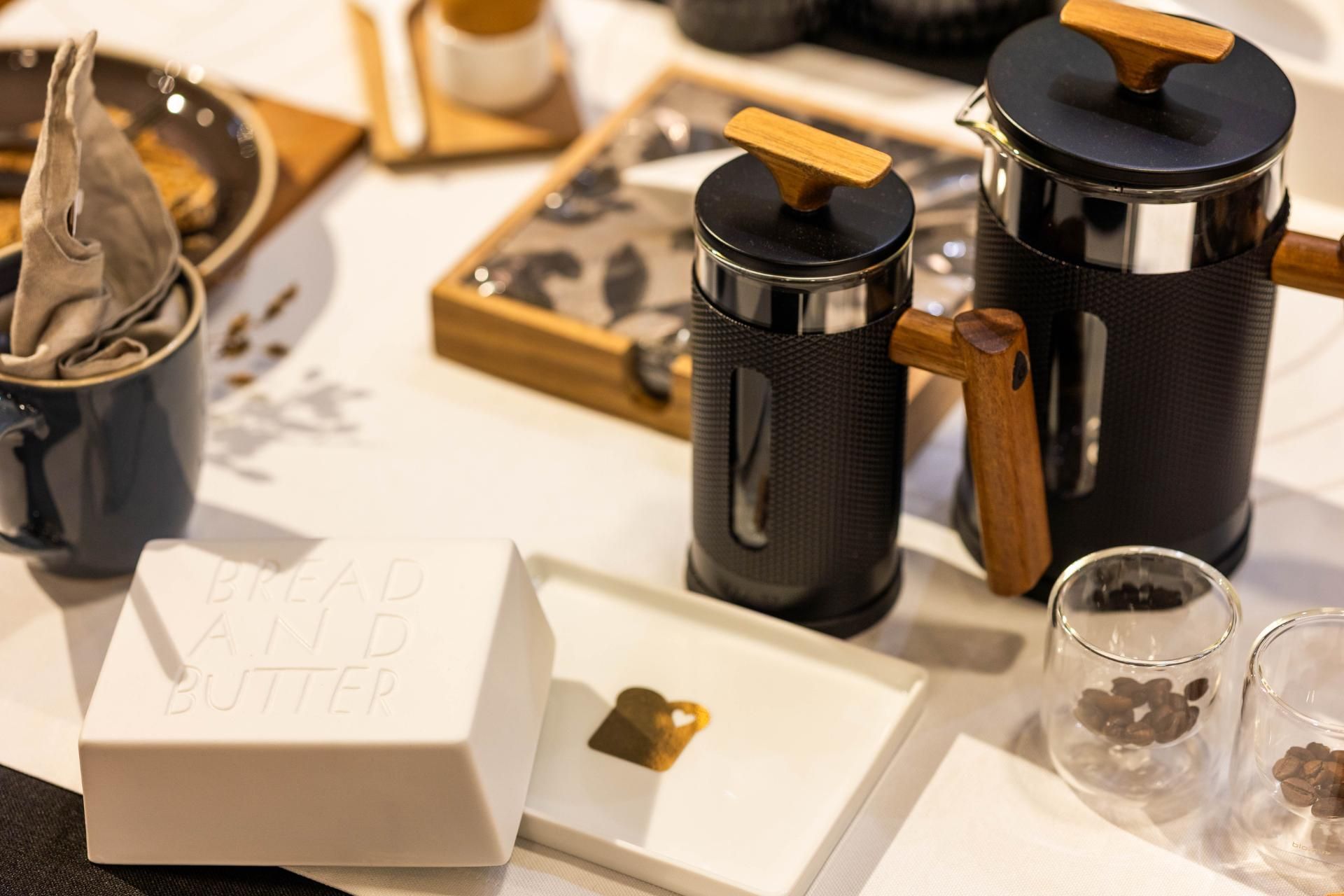 Kaffee-Setup: French Press mit Holzakzenten, weißes Geschirr mit Leckereien und blaue Tasse.