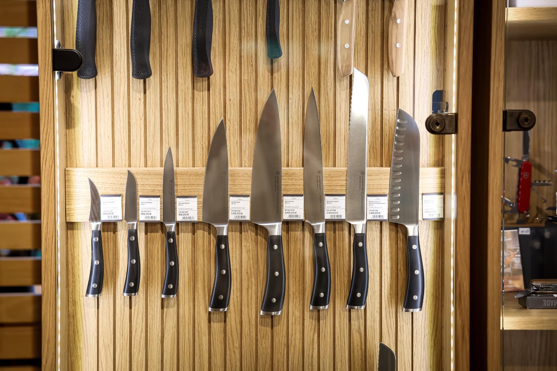 Auf einem Holzbrett ausgestellte Messer, verschiedene Größen und Formen, schwarze Griffe, silberne Klingen.