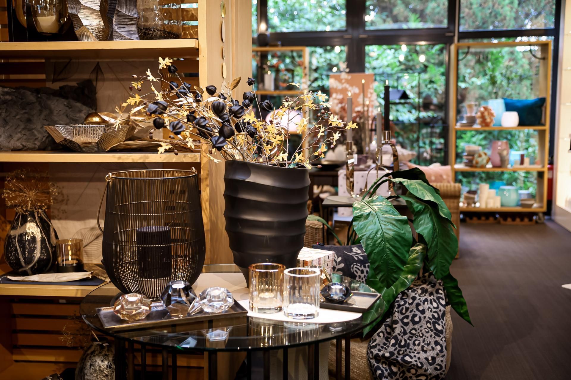 Innenansicht eines Ladens mit Vasen, Dekoration und Pflanzen. Tisch im Vordergrund, Regale im Hintergrund.