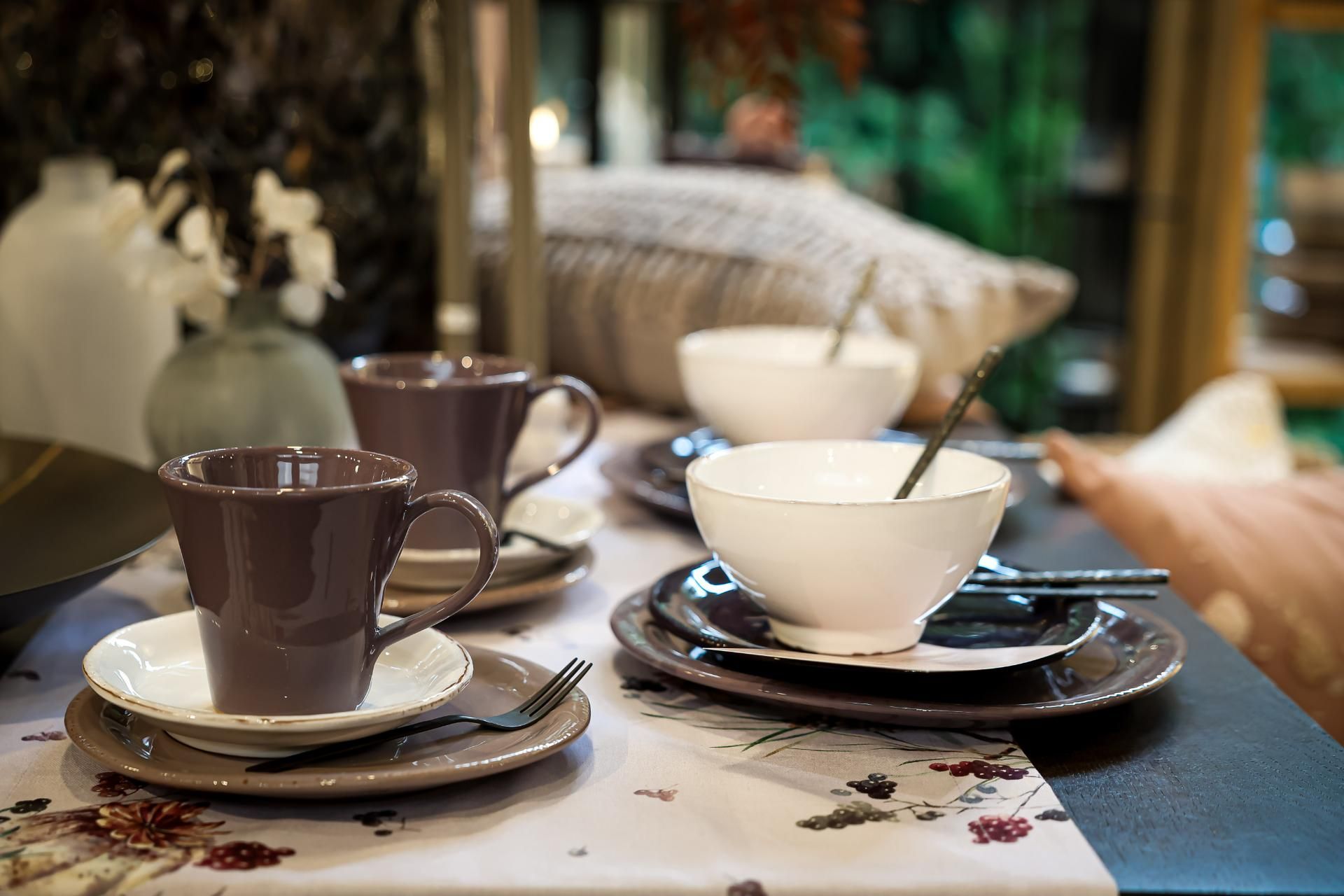 Tischgedeck mit braunen Bechern, weißen Schüsseln und Tellern auf einer geblümten Tischdecke.
