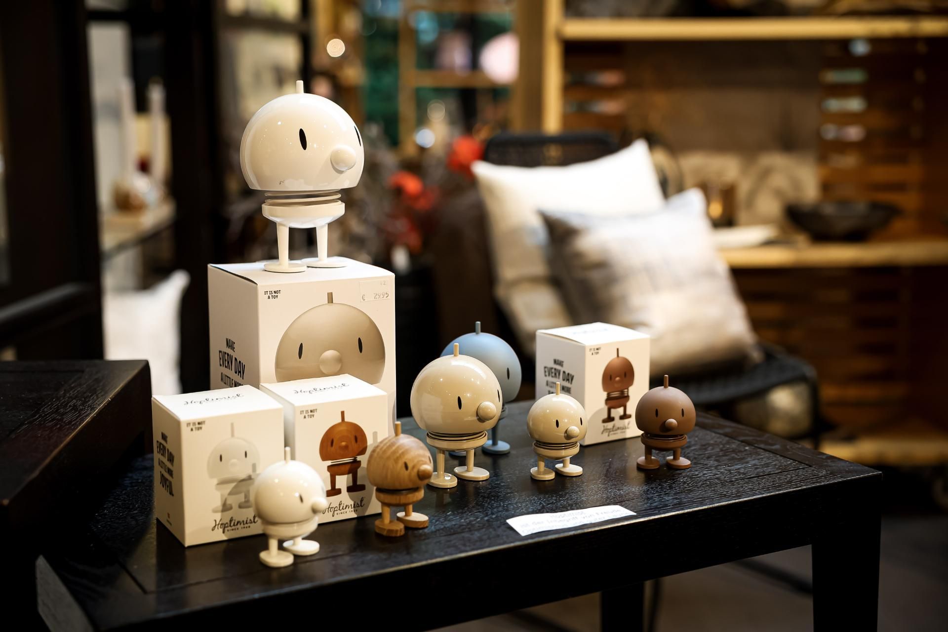 Ausstellung von Dekofiguren auf einem schwarzen Tisch; verschiedene Größen und Farben, im Hintergrund Kisten.