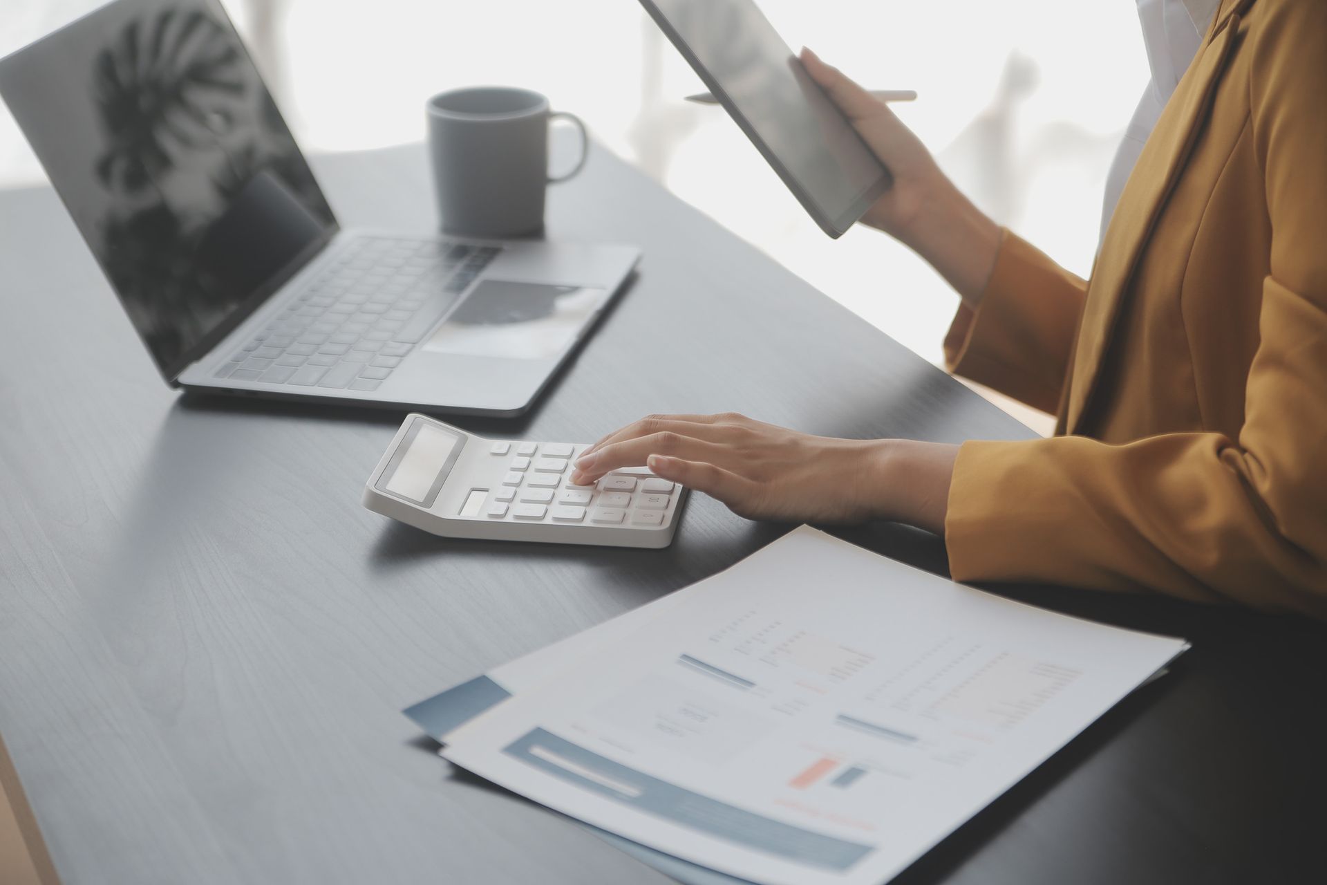 Una mujer está sentada en un escritorio usando una calculadora y una tableta.