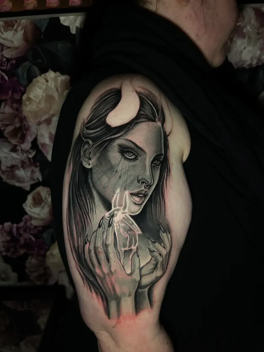 Tatuaje de un demonio femenino en un brazo; retrato en escala de grises, cuernos, sosteniendo una vela derretida.