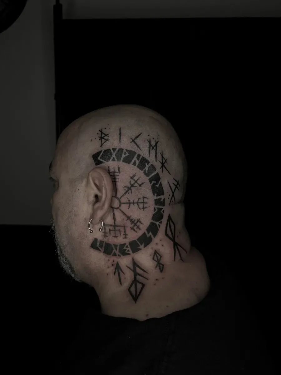Cabeza de hombre con un gran tatuaje negro de símbolos vikingos, incluida una brújula Vegvísir, en el costado y el cuello.