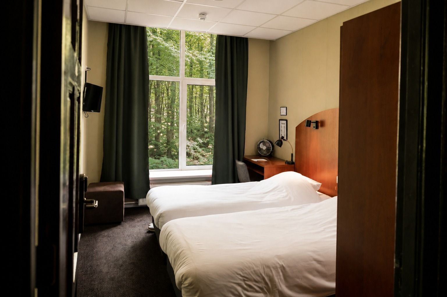 Hotelkamer met twee bedden, houten meubels en een groot raam met gordijnen.