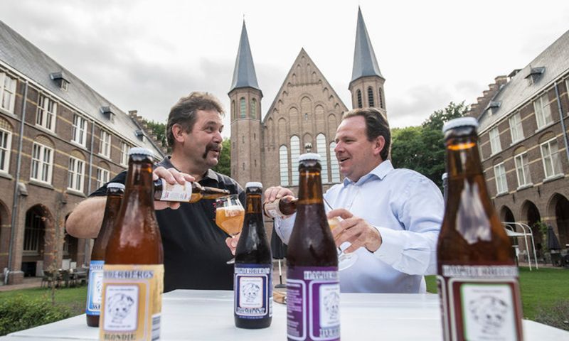 Twee mannen zitten aan een tafel met flessen bier voor een kerk.