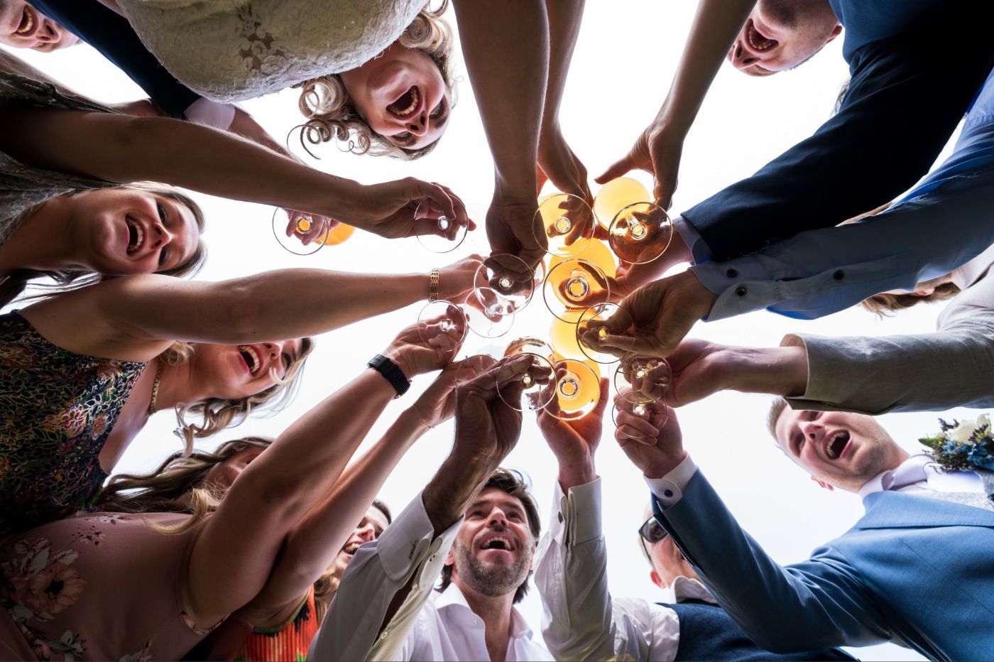 Vrienden klinken in een kring met bierglazen en kijken lachend naar de camera in de buitenlucht.