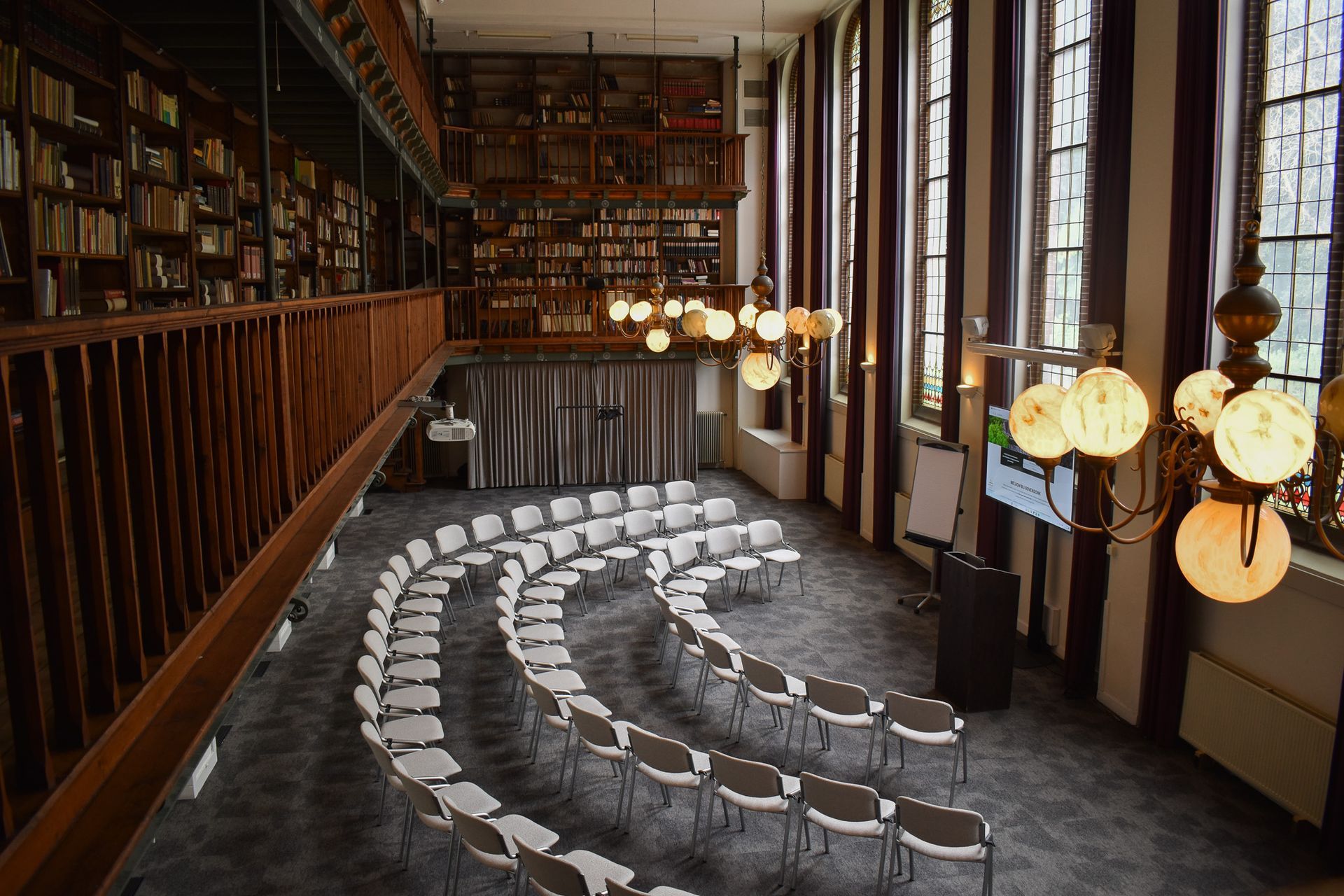 Authentieke zaal met hoge plafonds, grote glas-in-loodramen en moderne audiovisuele apparatuur.