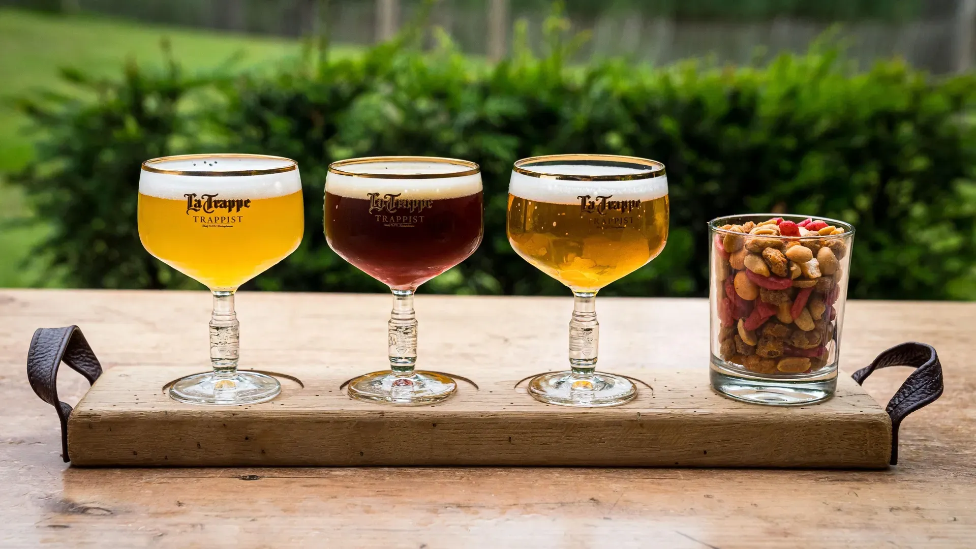 Drie glazen bier staan op een houten dienblad op een tafel.