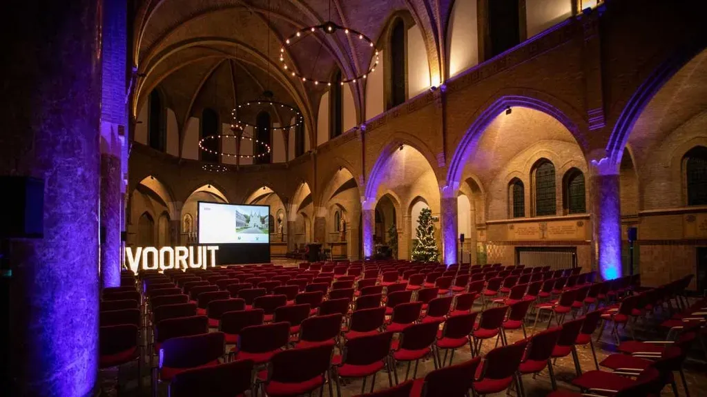 Een groot auditorium gevuld met rode stoelen en een groot scherm.