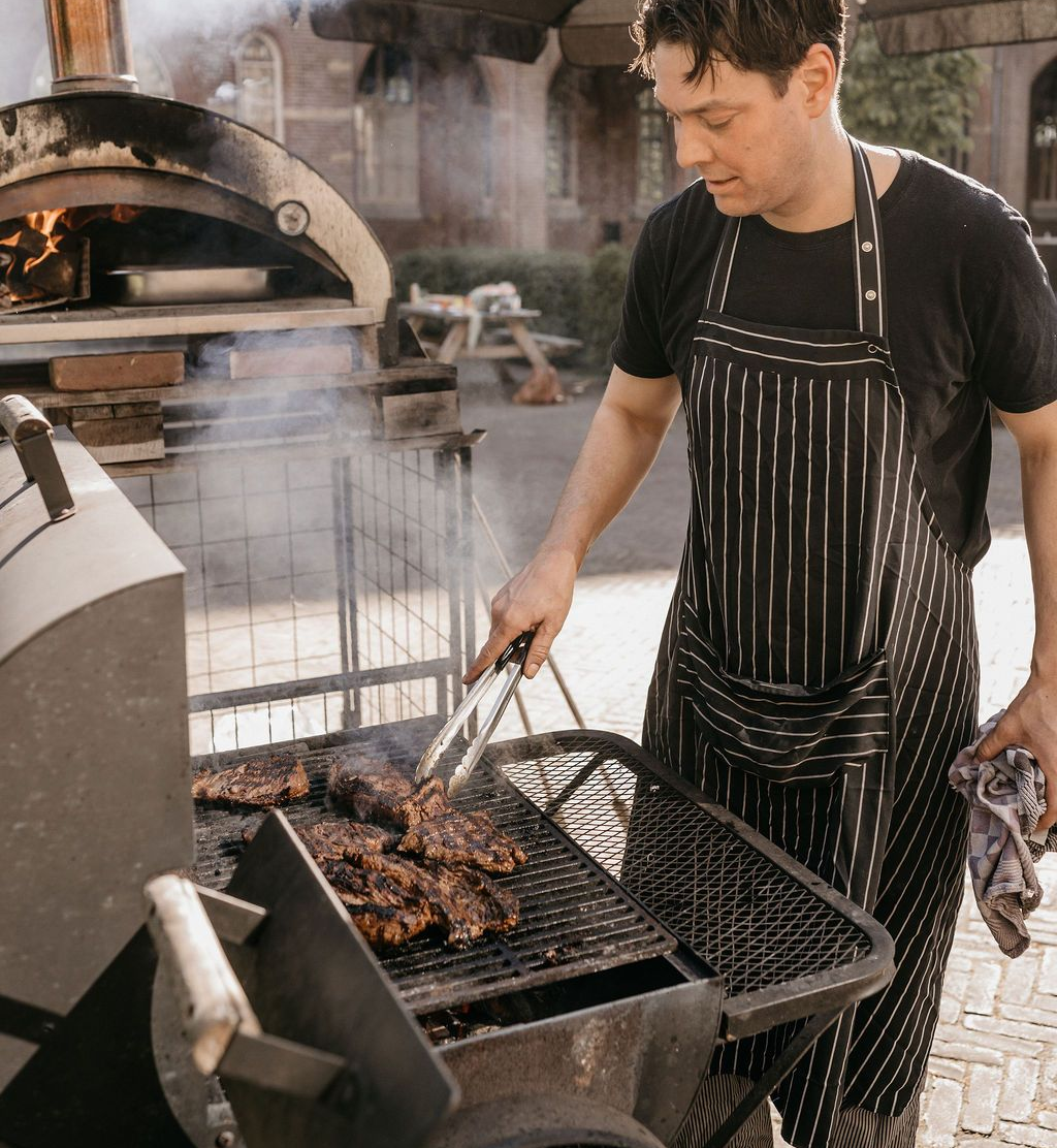 Een kok aan die vlees aan het bakken in op een barbeque in de binnentuin van Bovendonk
