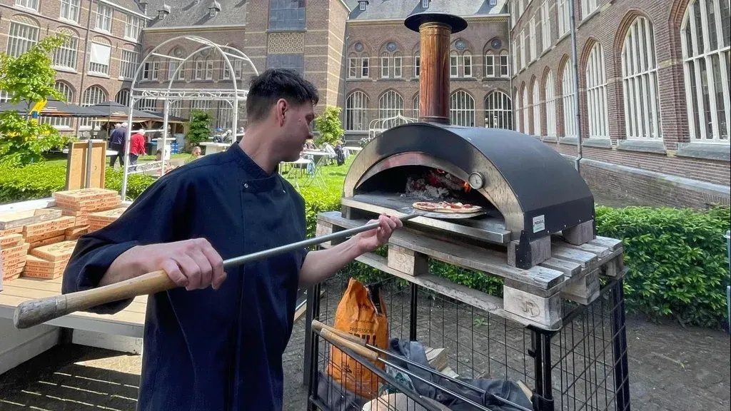 Een man zet een pizza in een pizzaoven buiten.