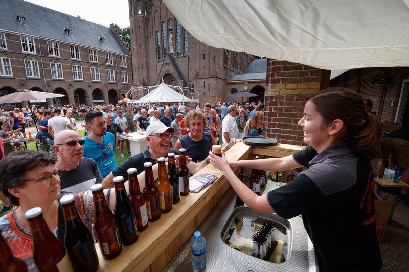 Een barvrouw serveert drankjes van een biertap op een drukbezocht bierfestival in onze binnentuin. 