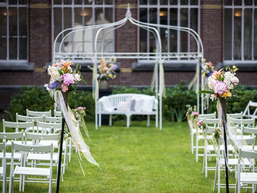 Een rij stoelen staat opgesteld voor een prieel versierd met bloemen.