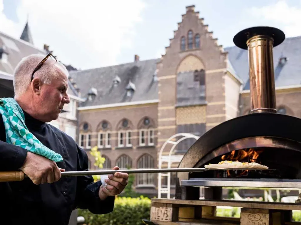 Een man kookt eten in een pizzaoven voor een gebouw.
