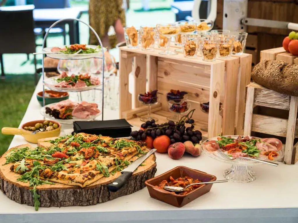 Een buffet met een pizza, druiven en ander eten erop.