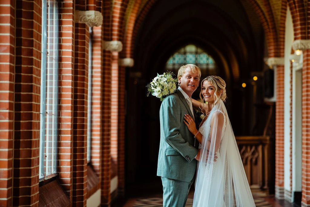 Bruid en bruidegom omhelzen elkaar voor de Kapel, terwijl de sluier van de bruid in de wind wappert.