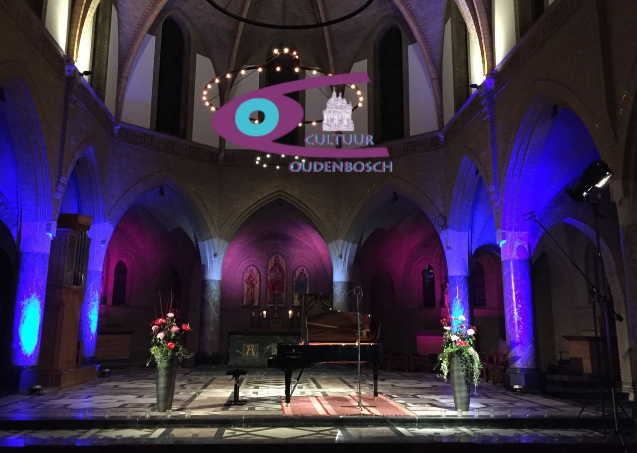 Een groep mensen die viool en cello spelen voor een bord met de tekst Oudenbosch