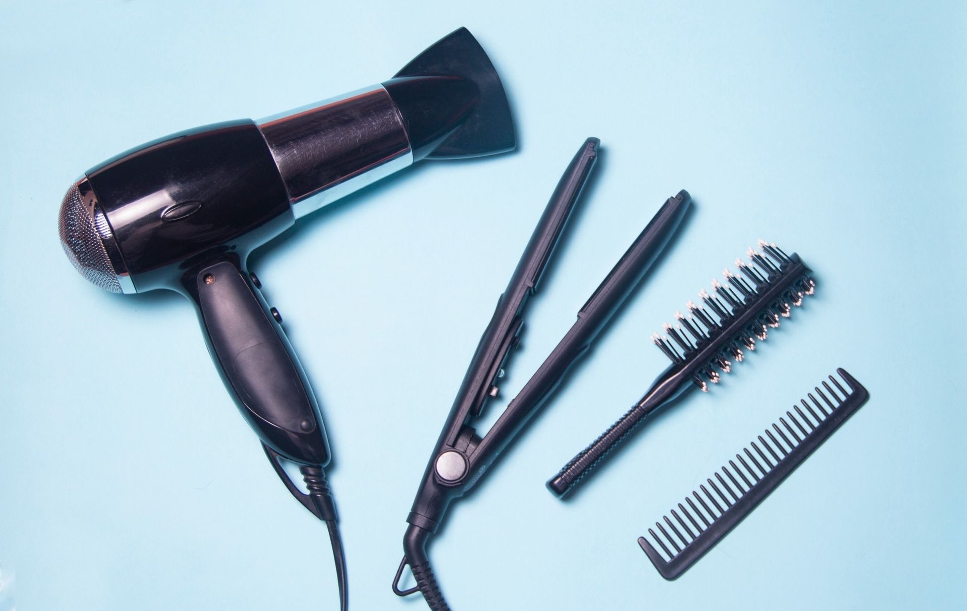 Un secador de pelo, una plancha de pelo y un peine están sobre una superficie azul.