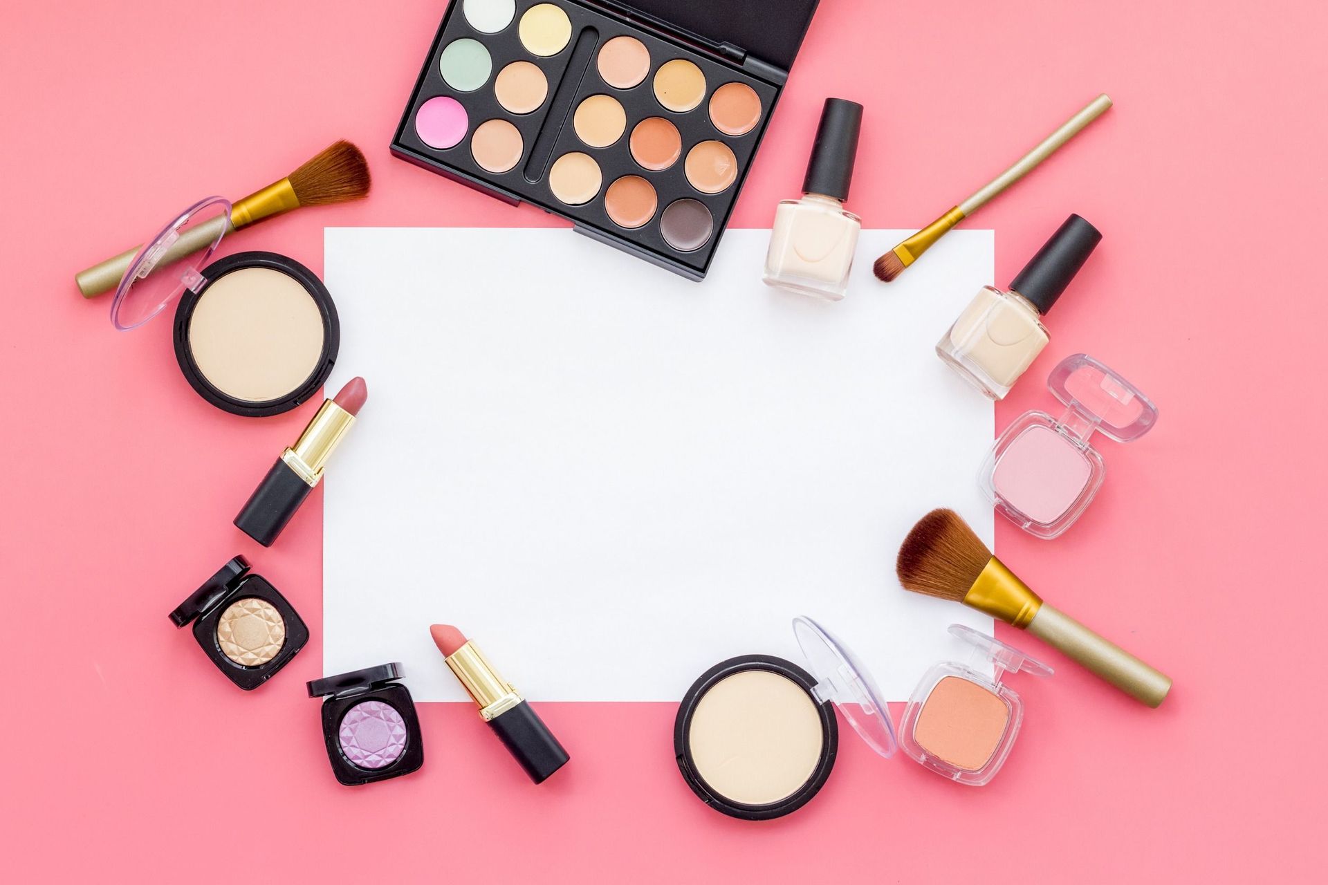 Una variedad de productos de maquillaje están dispuestos en un círculo sobre un fondo rosa.