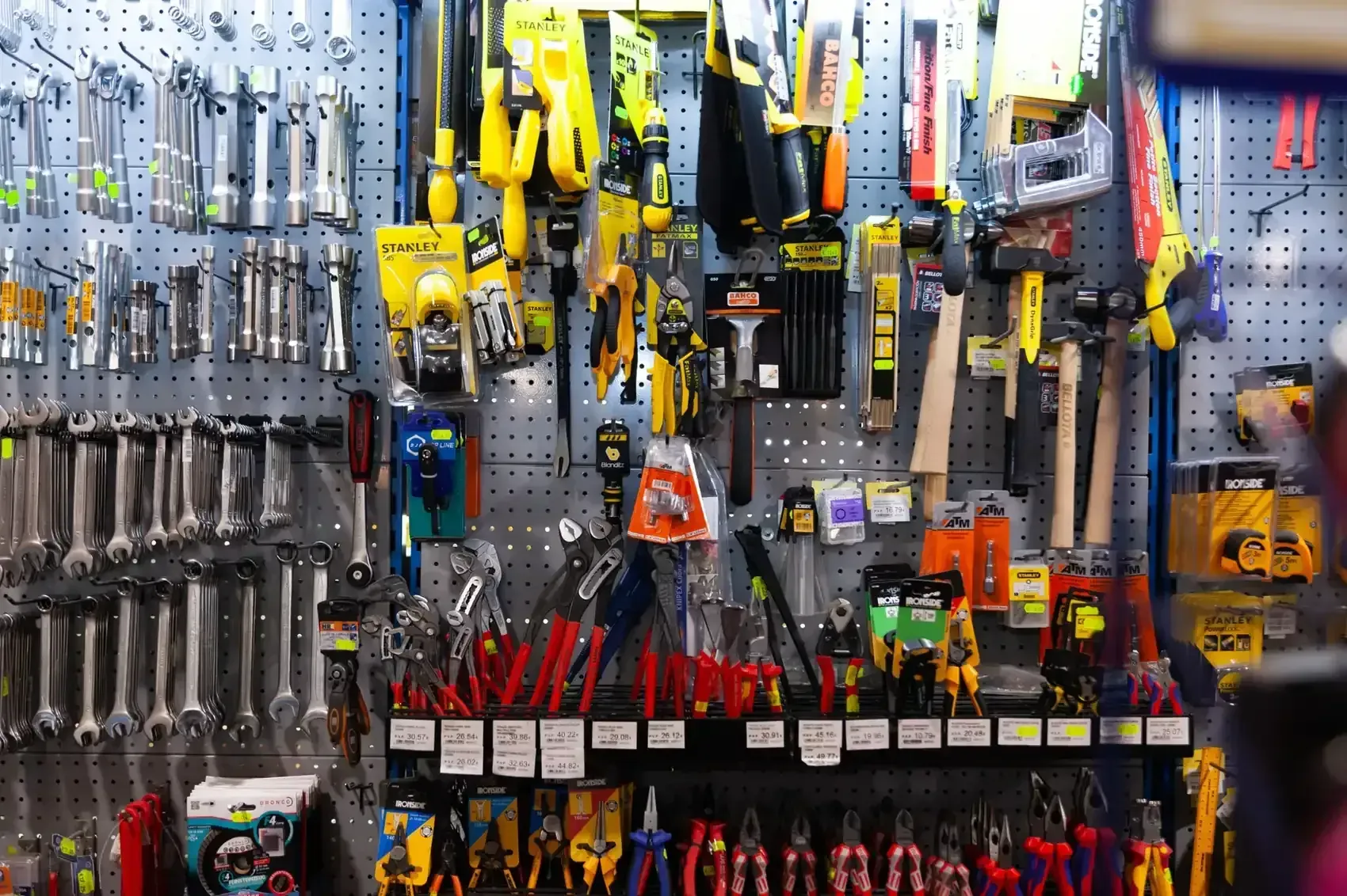 Una pared de exhibición comercial que muestra una variedad de herramientas manuales, incluyendo llaves inglesas, alicates y martillos, en ganchos de un panel perforado.