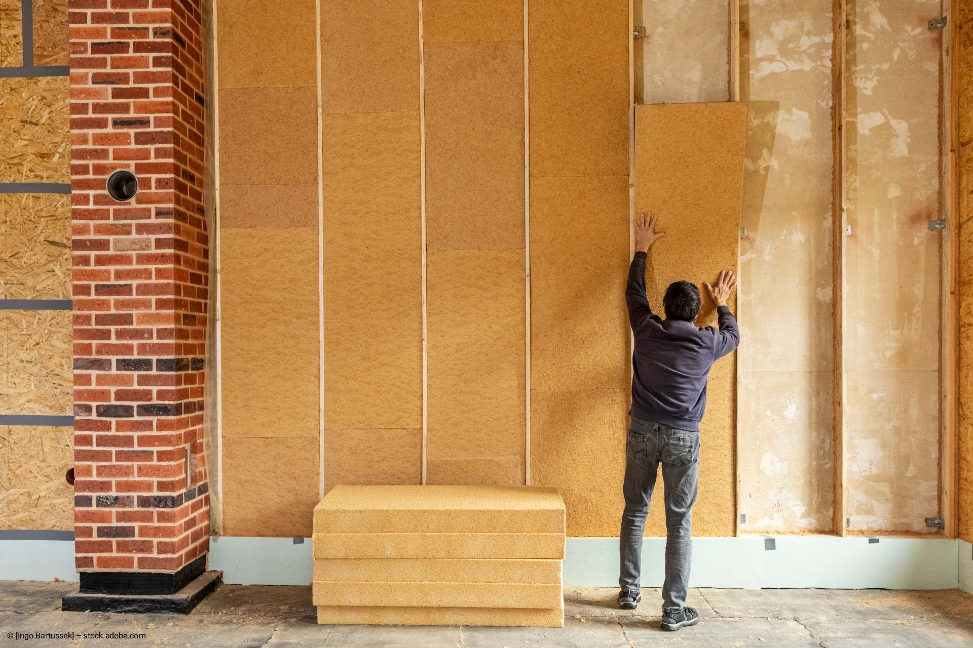 Eine Person montiert Korkdämmplatten an einer Wand in einem im Bau befindlichen Gebäude.