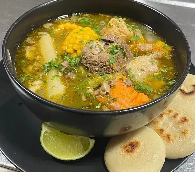 Un tazón de sopa con carne, maíz, zanahorias y patatas en un plato.