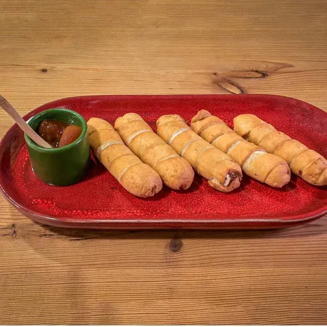 Un plato rojo cubierto con palitos de pan y un tazón pequeño de salsa.
