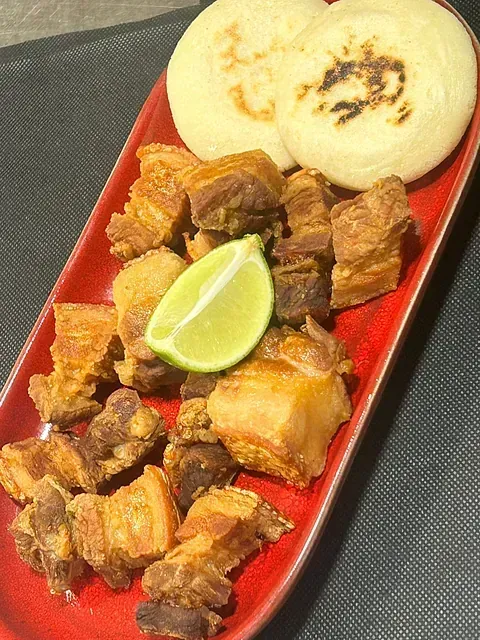Un plato rojo cubierto con carne, pan y una rodaja de lima.