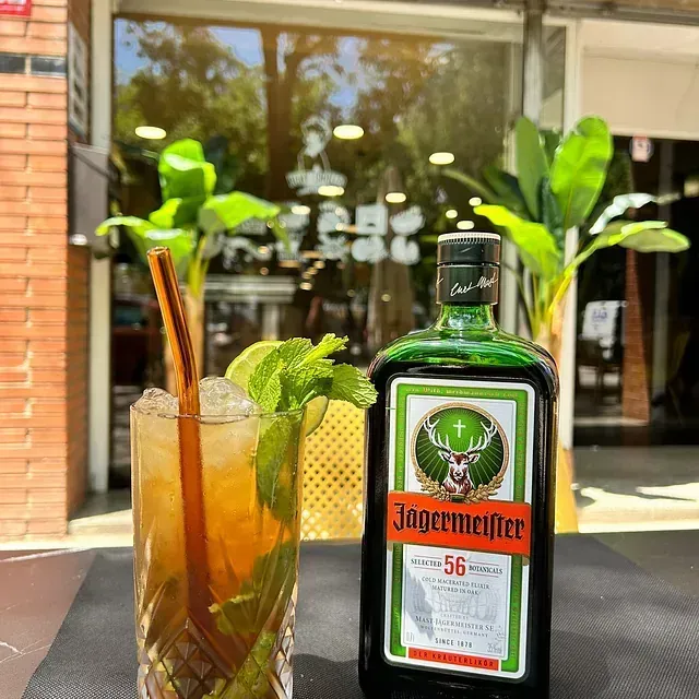 Una botella de Jägermeister junto a un vaso con pajita
