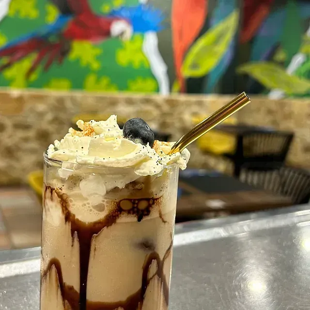 Un primer plano de un batido con crema batida y una pajita sobre una mesa.